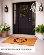 Front door with a customisable doormat featuring a monogram, flanked by potted plants. [VARIANT: TWO INITIALS / NO BORDER]