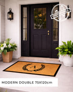 Front door with a customisable doormat featuring a monogram, flanked by potted plants. [VARIANT: SINGLE INITIAL / BORDER]