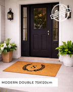 Front door with a customisable doormat featuring a monogram, flanked by potted plants. [VARIANT: SINGLE INITIAL / NO BORDER]