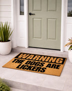 Doormat with 'Warning: The Dogs Are Lickers' text in front of a door. [VARIANT: DOGS / LICKERS]