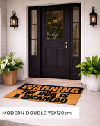 Front door with a humorous doormat and decorative plants. [VARIANT: DOG / DICKHEAD]