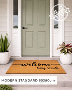 Doormat with 'welcome Airbnb Name' text in front of a green door, with potted plants on either side. [VARIANT: STANDARD]