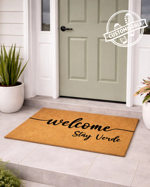 Doormat with 'welcome stay verde' text in front of a green door, with 'Customizable' label. [VARIANT: STANDARD]