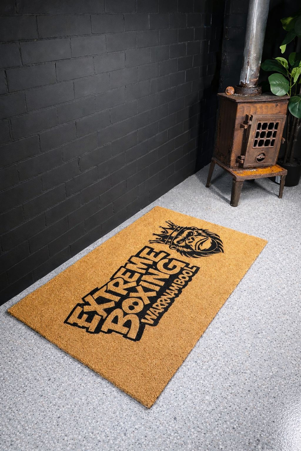 Doormat with 'Extreme Boxing' text on a gray floor against a black brick wall.