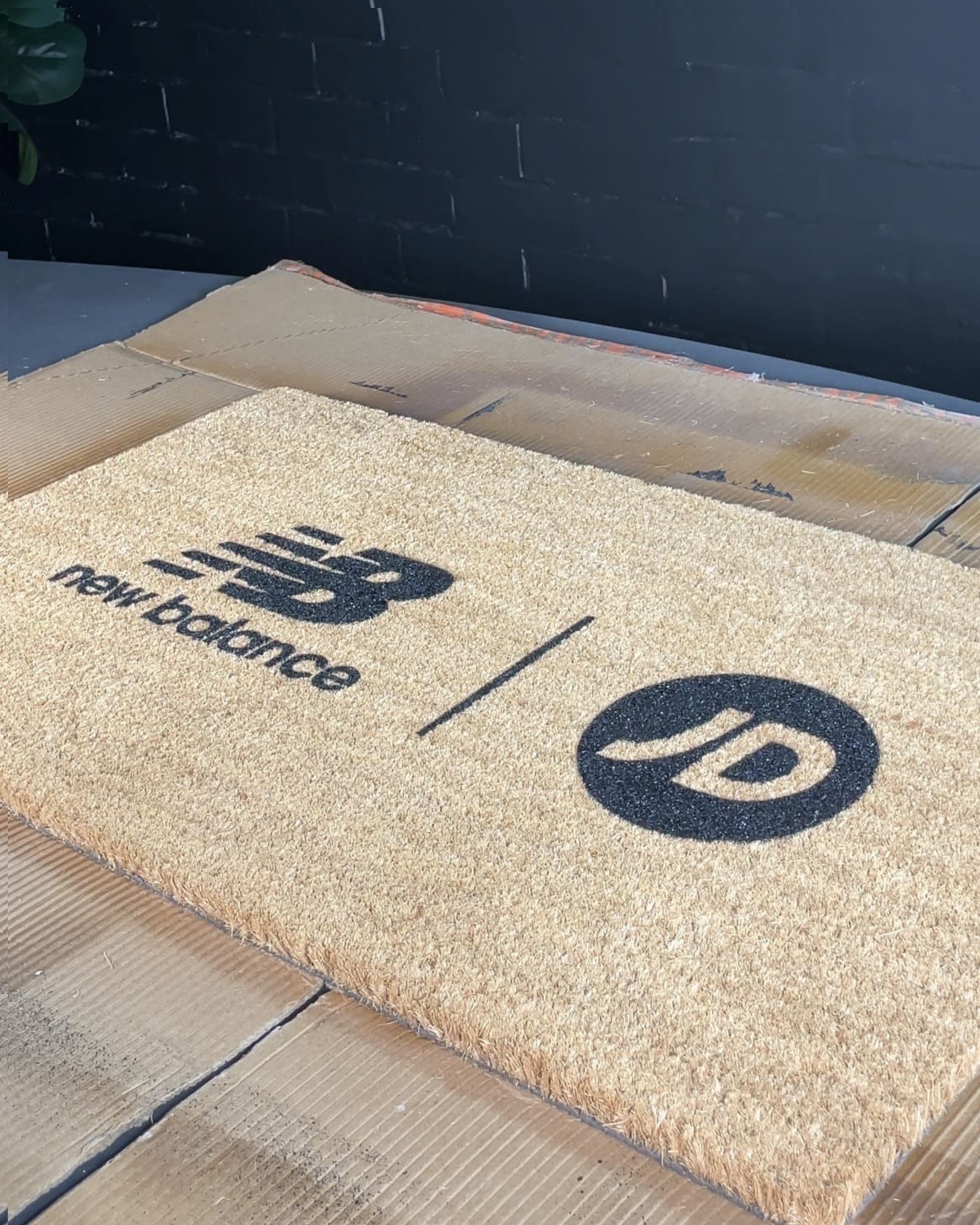 Doormat with New Balance and JD Sports logos on a tiled floor.