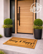 Doormat with text in front of a modern wooden door with plants on either side.