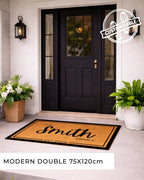 Front door with a personalized doormat and decorative plants. [VARIANT: BORDER-EST]