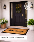 Front door with a doormat featuring 'The Johnson Family' text, flanked by potted plants. [VARIANT: BORDER-NO-EST]
