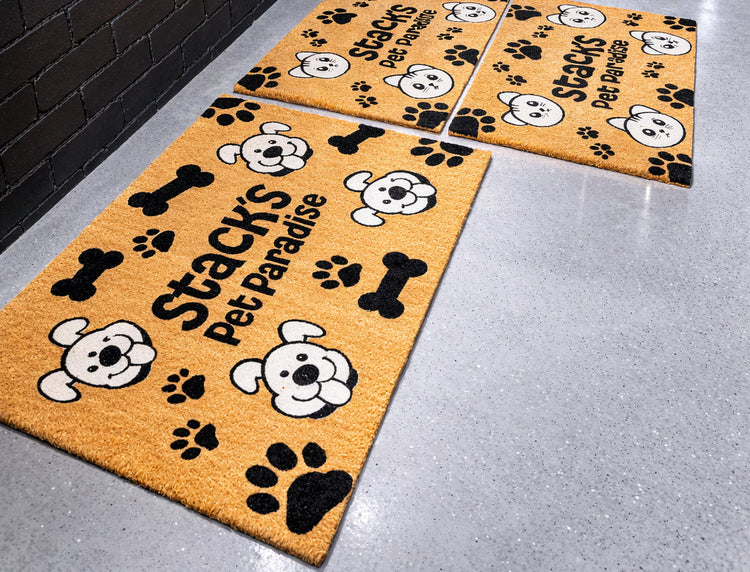 Set of three doormats with paw prints and 'Stacy's Pet Paradise' text on a gray floor.