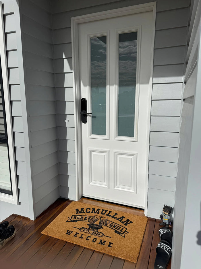 Front door of a house with a doormat featuring 'McMullan Farms Grill Welcome' text.