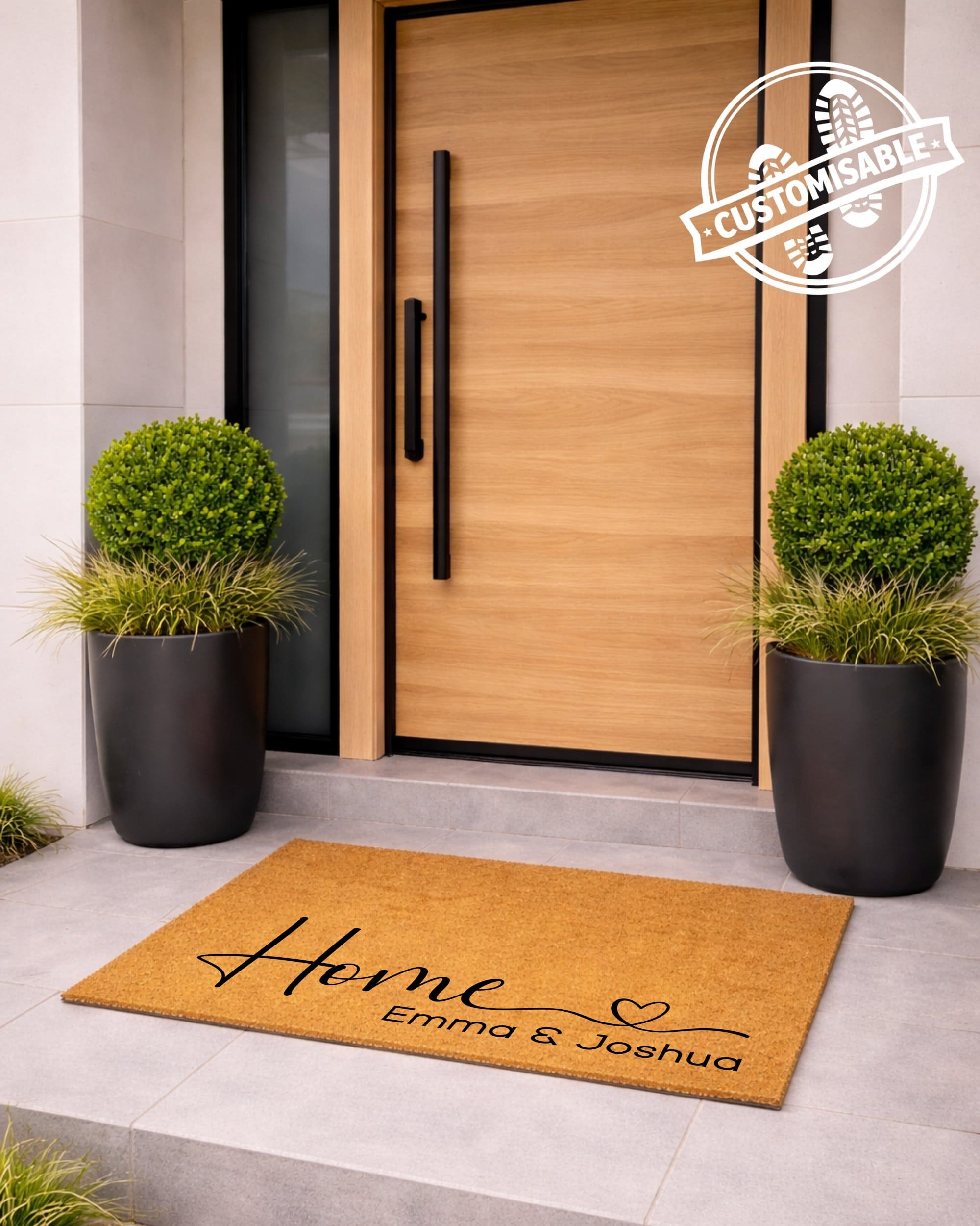 Doormat with 'Home Emma & Joshua' text in front of a modern wooden door with planters on either side.
