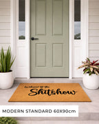Doormat with 'Welcome to the Shitshow' text in front of a green door.