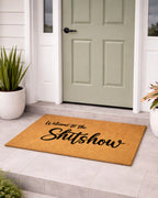 Doormat with 'Welcome to the Shitshow' text in front of a green door.